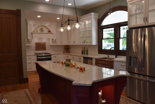 kitchen featuring light stone counters, a center island, stainless steel appliances, decorative light fixtures, and dark hardwood / wood-style flooring