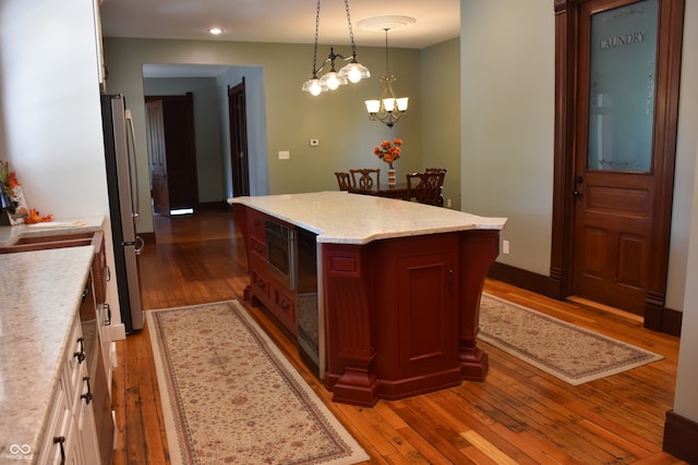 kitchen with white cabinets, hanging light fixtures, a kitchen island, appliances with stainless steel finishes, and hardwood / wood-style floors