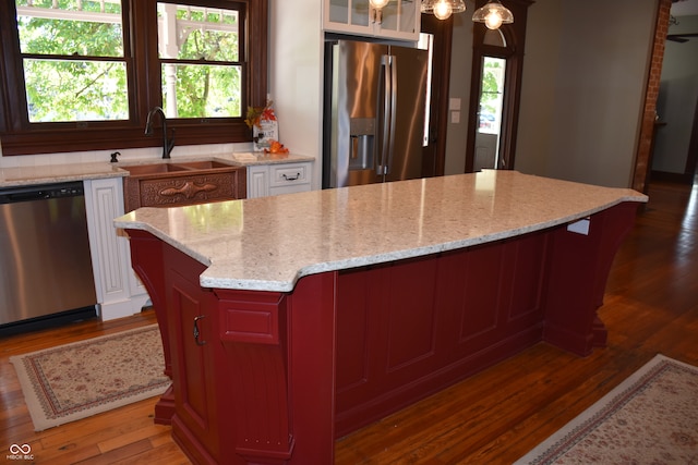 kitchen with sink, a kitchen island, dark wood-type flooring, stainless steel appliances, and light stone countertops