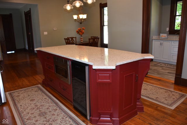 kitchen with pendant lighting, beverage cooler, a center island, dark hardwood / wood-style floors, and a notable chandelier