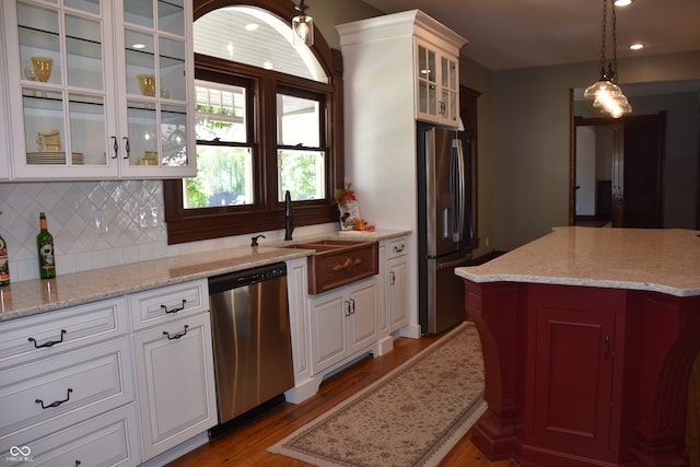 kitchen with appliances with stainless steel finishes, tasteful backsplash, pendant lighting, wood-type flooring, and sink