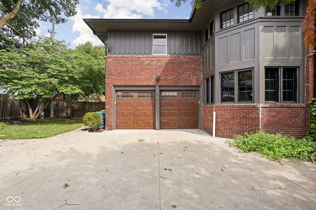 view of home's exterior with driveway, fence, board and batten siding, an attached garage, and brick siding