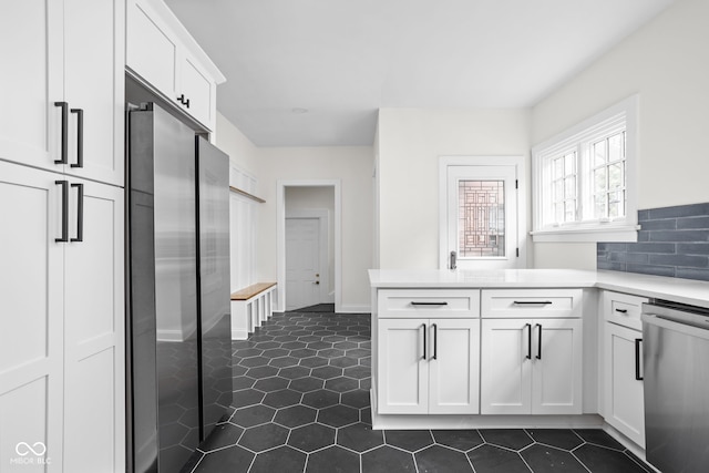 kitchen with dark tile patterned flooring, kitchen peninsula, stainless steel appliances, decorative backsplash, and white cabinets