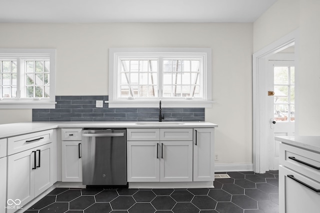 kitchen with dark tile patterned flooring, white cabinetry, stainless steel dishwasher, and sink