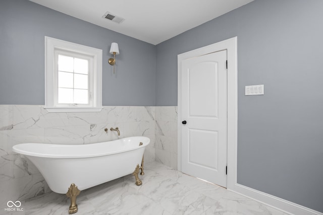 bathroom featuring visible vents, a soaking tub, marble finish floor, and a wainscoted wall