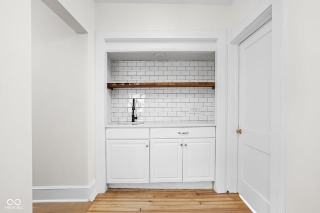 bar with a sink, light wood-type flooring, baseboards, and tasteful backsplash