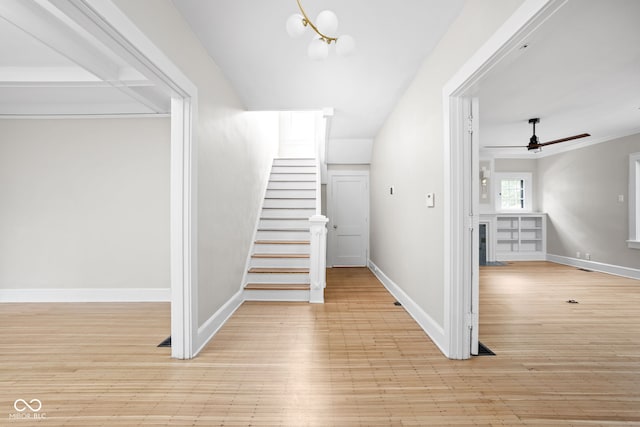 stairway with ornamental molding, hardwood / wood-style floors, and ceiling fan with notable chandelier