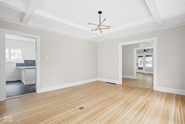 spare room with a wealth of natural light, light hardwood / wood-style flooring, coffered ceiling, and ceiling fan with notable chandelier