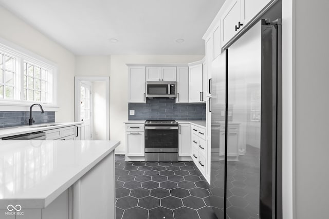 kitchen featuring dark tile patterned flooring, white cabinetry, sink, decorative backsplash, and appliances with stainless steel finishes