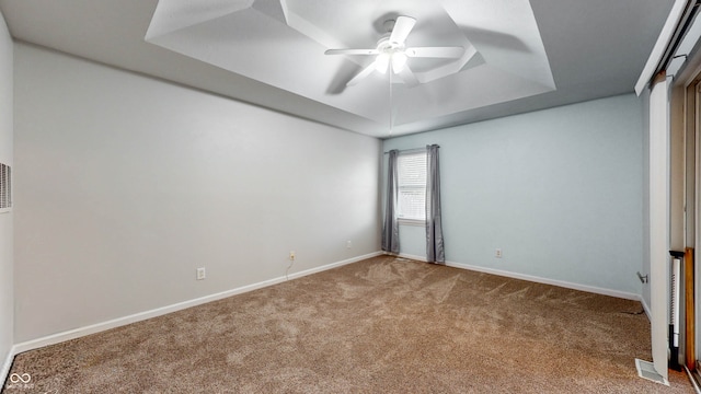 carpeted spare room with a raised ceiling and ceiling fan