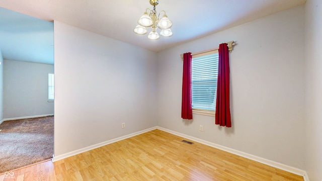 empty room featuring hardwood / wood-style flooring, a wealth of natural light, and an inviting chandelier