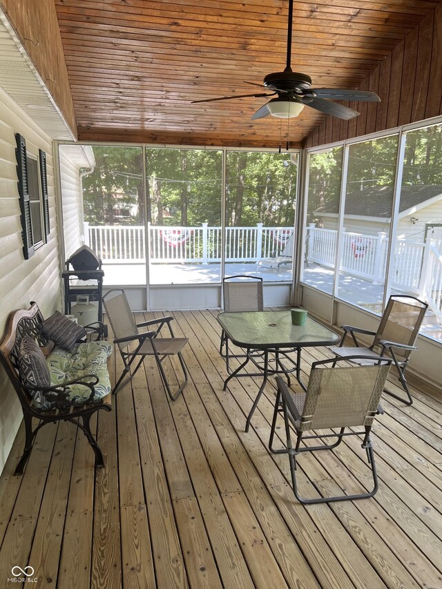 unfurnished sunroom featuring wood ceiling, ceiling fan, and a healthy amount of sunlight