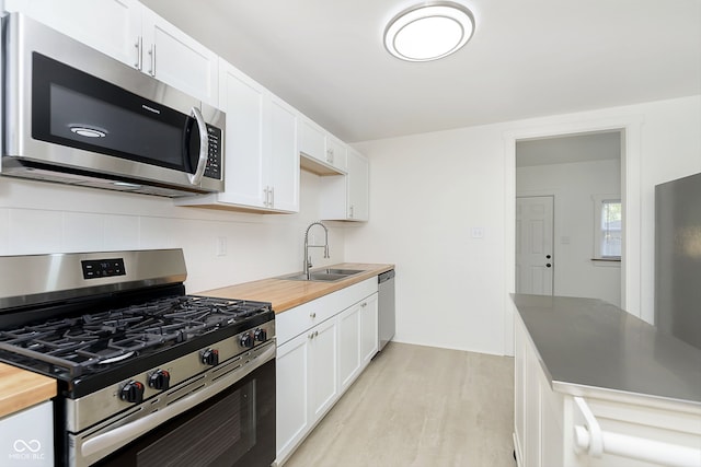 kitchen featuring stainless steel appliances, sink, wood counters, and white cabinetry