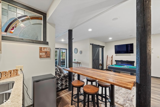 bar with a barn door, stainless steel refrigerator, and hardwood / wood-style floors