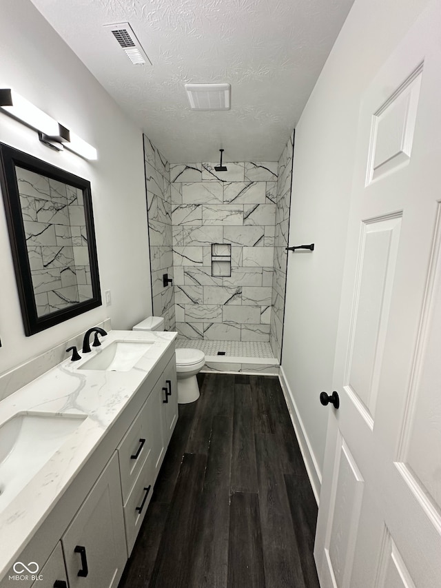 bathroom featuring a textured ceiling, a tile shower, hardwood / wood-style floors, vanity, and toilet