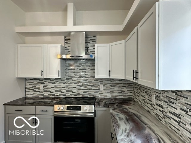 kitchen featuring white cabinets, wall chimney exhaust hood, stainless steel stove, and tasteful backsplash