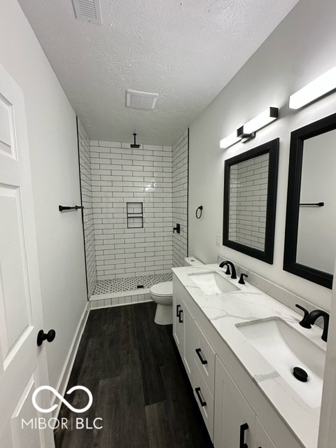 bathroom with wood-type flooring, a textured ceiling, toilet, and tiled shower