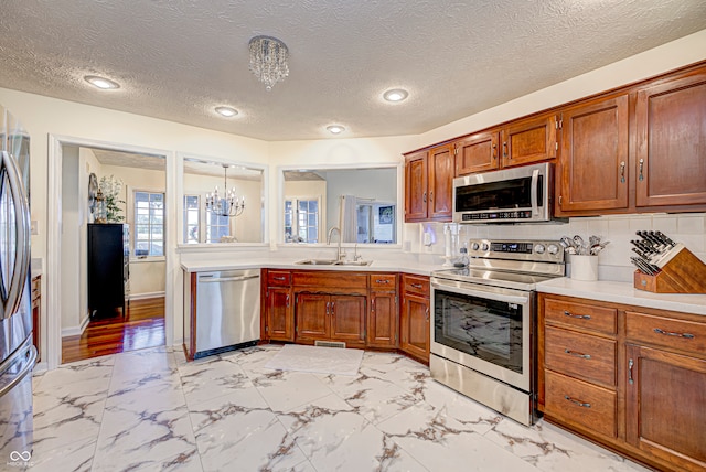 kitchen featuring decorative light fixtures, a notable chandelier, tasteful backsplash, stainless steel appliances, and sink