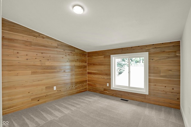 carpeted empty room featuring vaulted ceiling and wooden walls