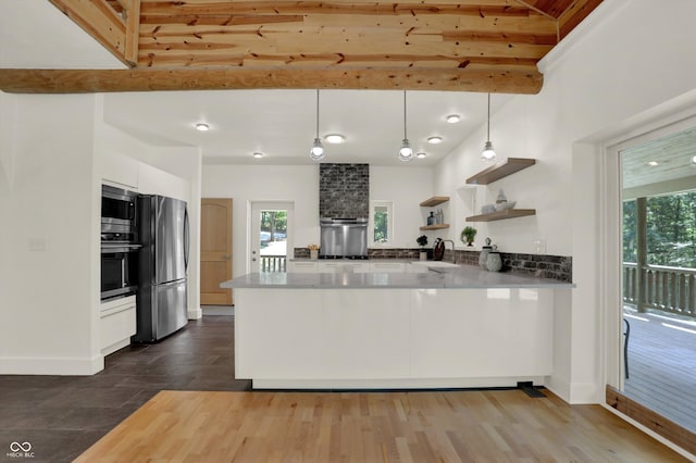 kitchen with appliances with stainless steel finishes, white cabinetry, hardwood / wood-style flooring, and kitchen peninsula