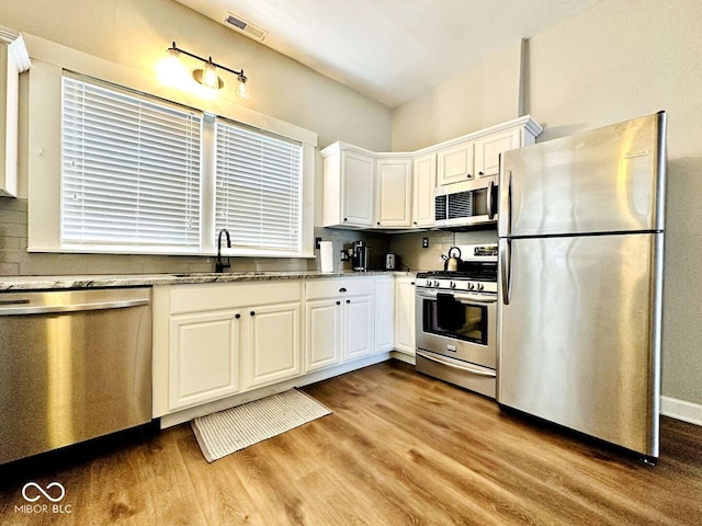 kitchen featuring light wood-type flooring, white cabinetry, light stone counters, sink, and appliances with stainless steel finishes