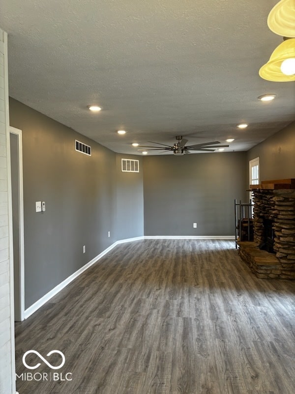 unfurnished living room with a textured ceiling, dark wood-type flooring, ceiling fan, and a fireplace