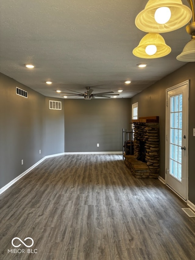 unfurnished living room featuring a textured ceiling, ceiling fan, dark hardwood / wood-style flooring, and a fireplace