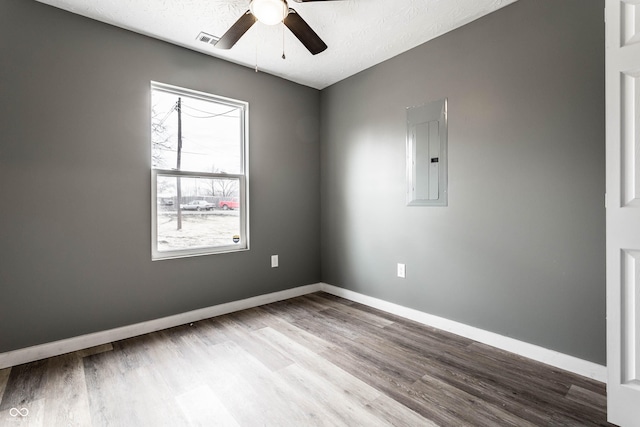 empty room featuring baseboards, electric panel, visible vents, and wood finished floors