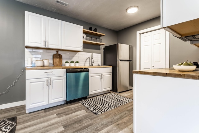 kitchen with butcher block countertops, visible vents, light wood-type flooring, freestanding refrigerator, and dishwasher