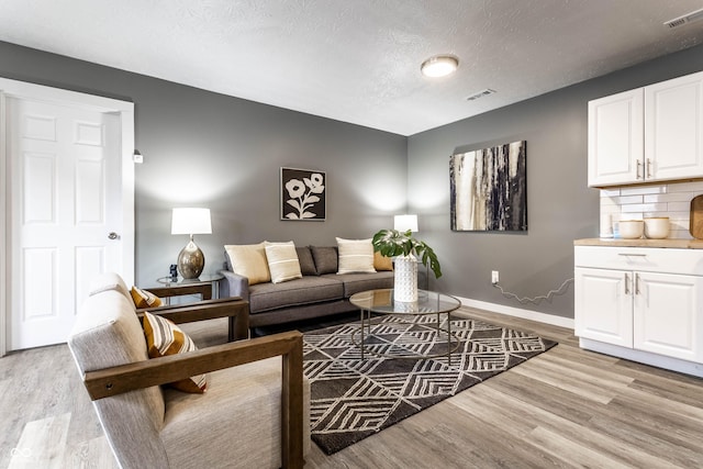 living room featuring a textured ceiling, light wood finished floors, visible vents, and baseboards