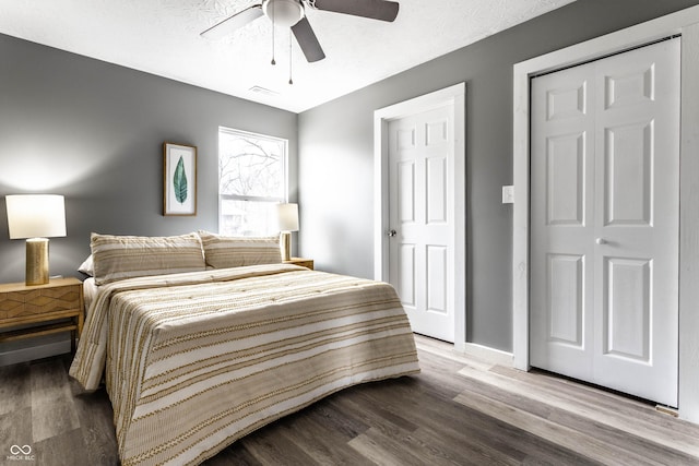 bedroom featuring ceiling fan, a textured ceiling, wood finished floors, visible vents, and baseboards