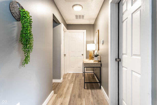 corridor with light wood-style floors, visible vents, a textured ceiling, and baseboards