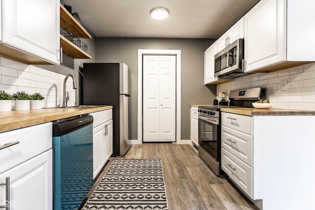 kitchen with stainless steel appliances, white cabinets, a sink, and wood counters