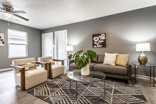 living area featuring baseboards, visible vents, ceiling fan, wood finished floors, and a textured ceiling