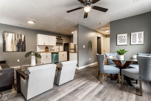 dining room with a textured ceiling, a ceiling fan, baseboards, light wood finished floors, and attic access