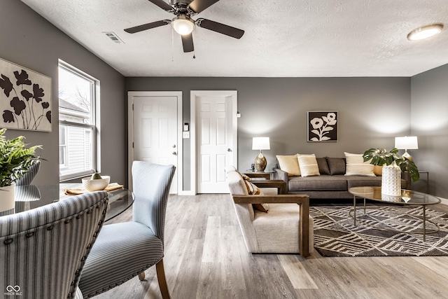 living area featuring baseboards, visible vents, ceiling fan, wood finished floors, and a textured ceiling