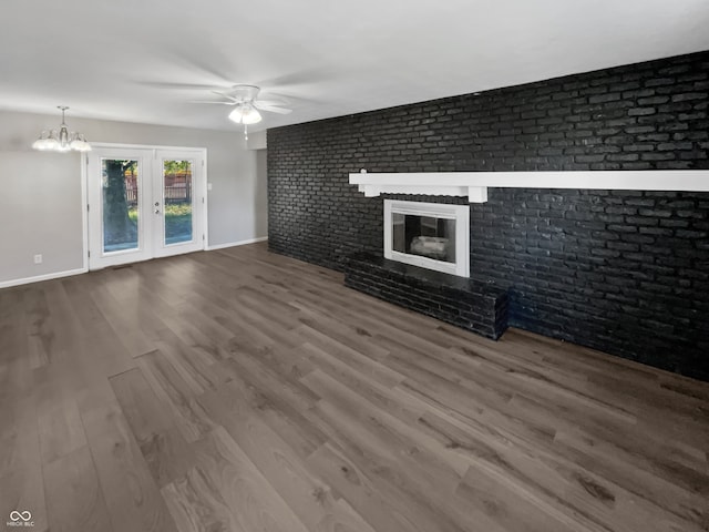 unfurnished living room featuring a fireplace, ceiling fan with notable chandelier, wood-type flooring, and brick wall