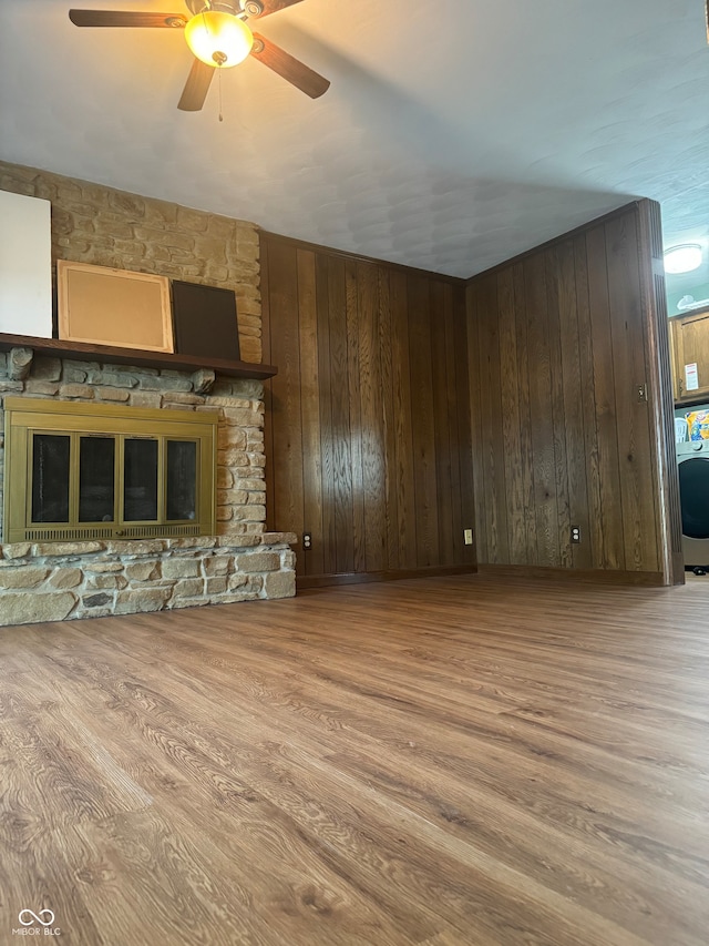 unfurnished living room featuring hardwood / wood-style flooring, wood walls, ceiling fan, and a stone fireplace