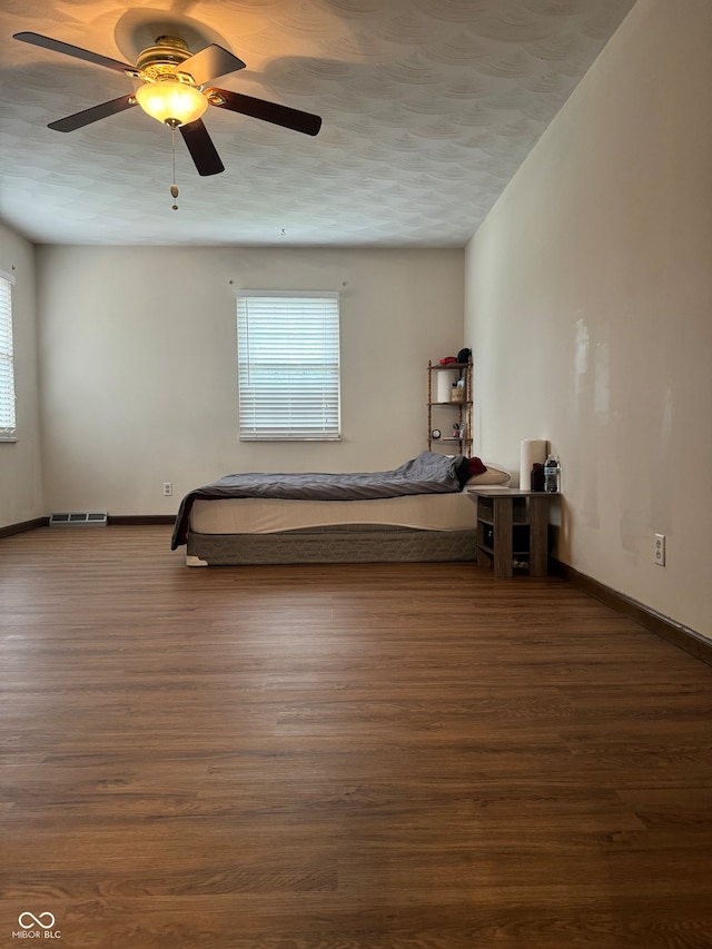 unfurnished bedroom featuring a textured ceiling, dark wood-type flooring, ceiling fan, and multiple windows