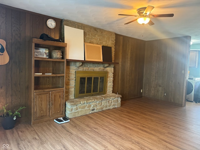 unfurnished living room with wooden walls, light hardwood / wood-style flooring, washer and dryer, a stone fireplace, and ceiling fan