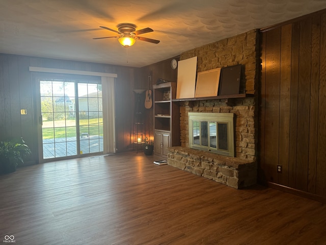 unfurnished living room featuring wood walls, ceiling fan, a fireplace, and dark hardwood / wood-style floors