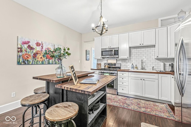 kitchen with dark wood finished floors, a sink, appliances with stainless steel finishes, wood counters, and tasteful backsplash