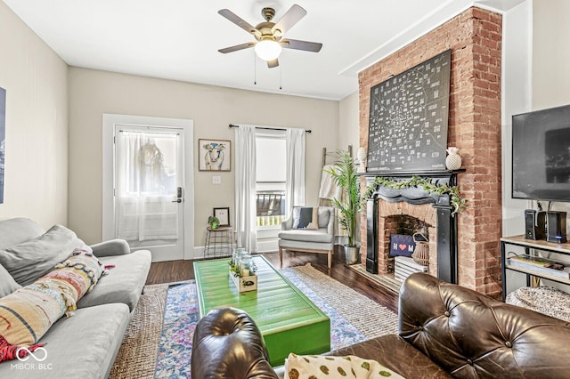 living area featuring ceiling fan, baseboards, a brick fireplace, and wood finished floors