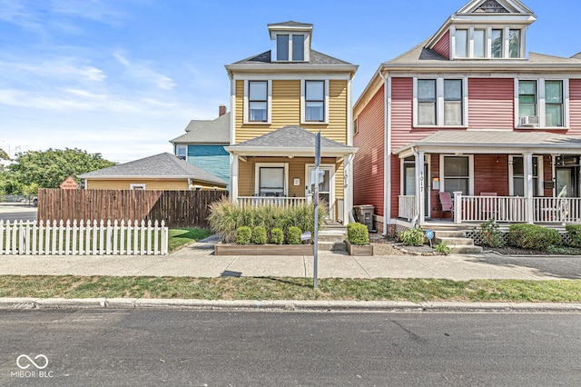 american foursquare style home featuring covered porch, cooling unit, a shingled roof, and fence