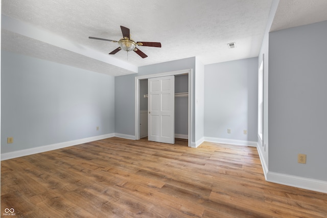 unfurnished bedroom with light wood-type flooring, a textured ceiling, ceiling fan, and a closet