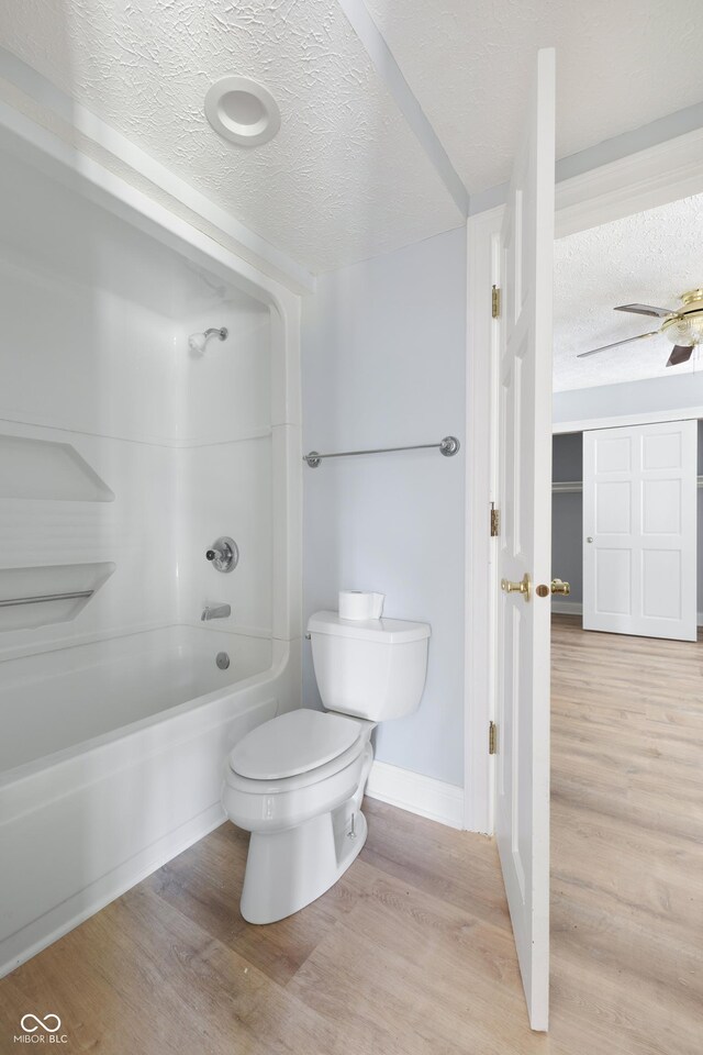 bathroom featuring hardwood / wood-style floors, toilet, tub / shower combination, ceiling fan, and a textured ceiling