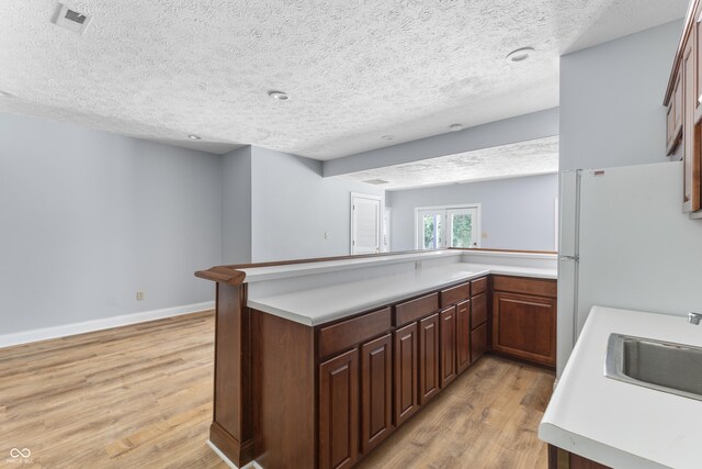 kitchen featuring sink, light hardwood / wood-style floors, kitchen peninsula, and a textured ceiling