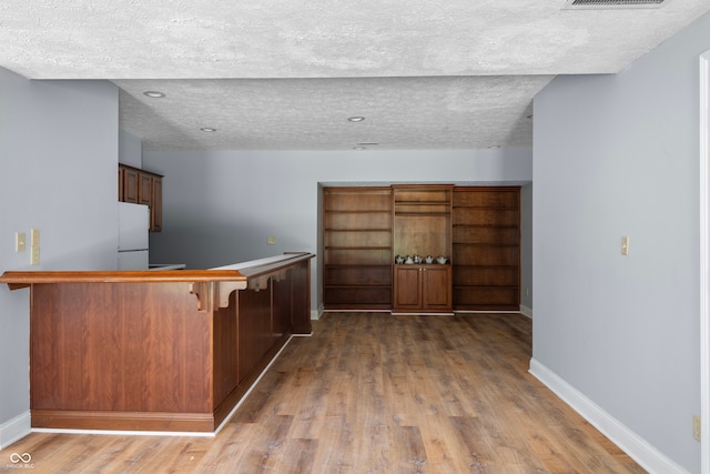 kitchen featuring white fridge, a textured ceiling, wood-type flooring, kitchen peninsula, and a breakfast bar area