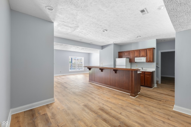 kitchen featuring white appliances, a breakfast bar area, a textured ceiling, and light hardwood / wood-style flooring