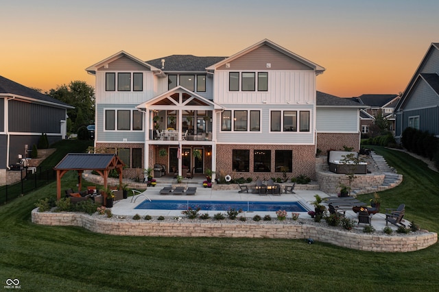 back house at dusk with a lawn, a patio, and a balcony